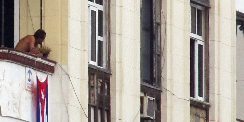 Hombre mirando hacia la calle desde un balcón de la Habanaa, Cuba. Historias de la Habana.